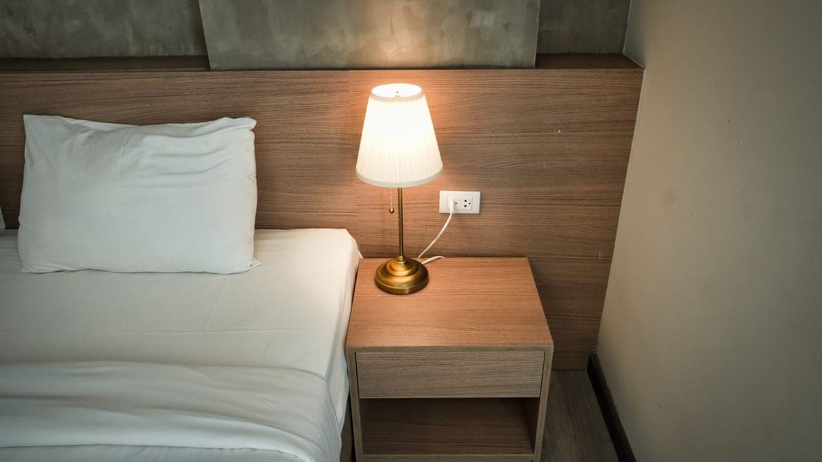 A lamp on a nightstand beside a bed in a dimly lit bedroom