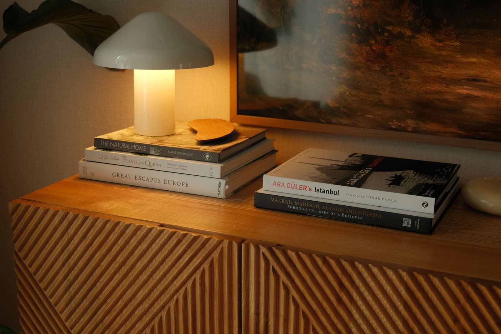 A small electric table lamp lit on a stack of books on a wooden sideboard