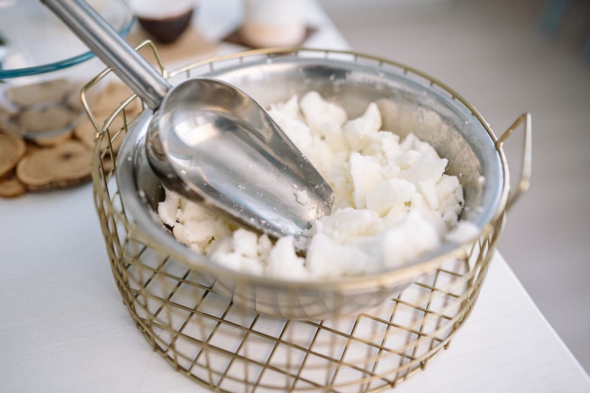 Soy wax flakes in a metal bowl with a scoop, on a pale table